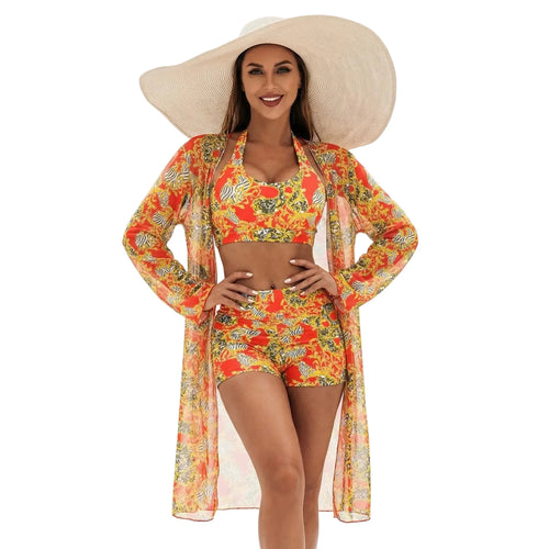 Femme portant un ensemble de plage trois pièces avec un haut licou, un short et un kimono assortis aux motifs baroques orange et jaune, complété par un grand chapeau de paille blanc.